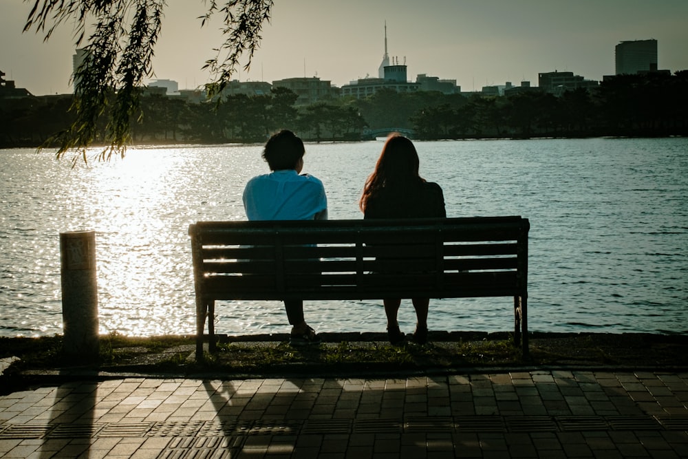 2 person sitting on bench near body of water during daytime