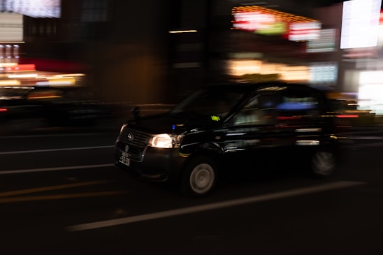 A modern taxi driving through a city street at night.