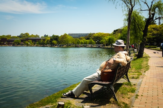 woman in white jacket sitting on brown wooden chair near body of water during daytime in Ōhorikōen Japan