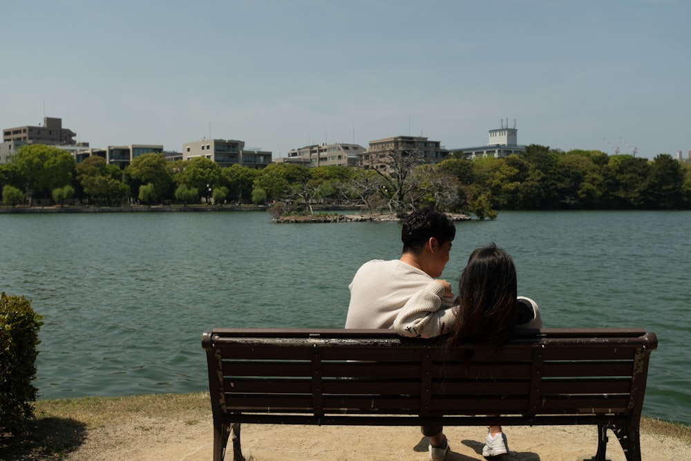 낮 동안 수역 근처의 갈색 나무 벤치에 앉아 있는 커플