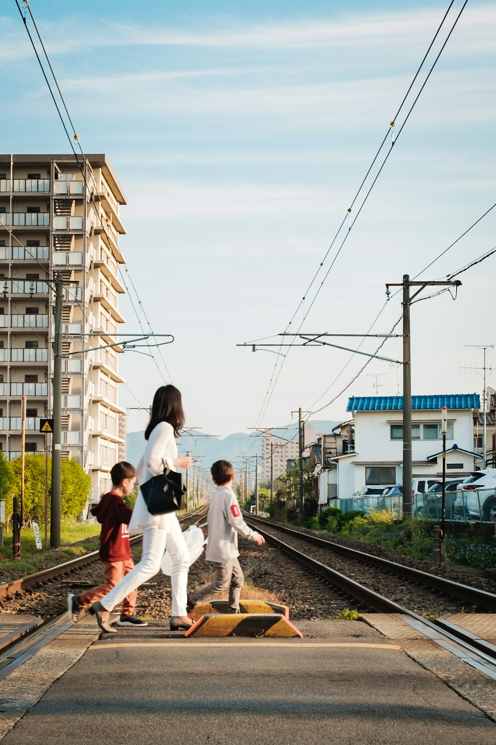 白い長袖シャツと白いズボンを着た女性が昼間、電車のレールの上に立っている