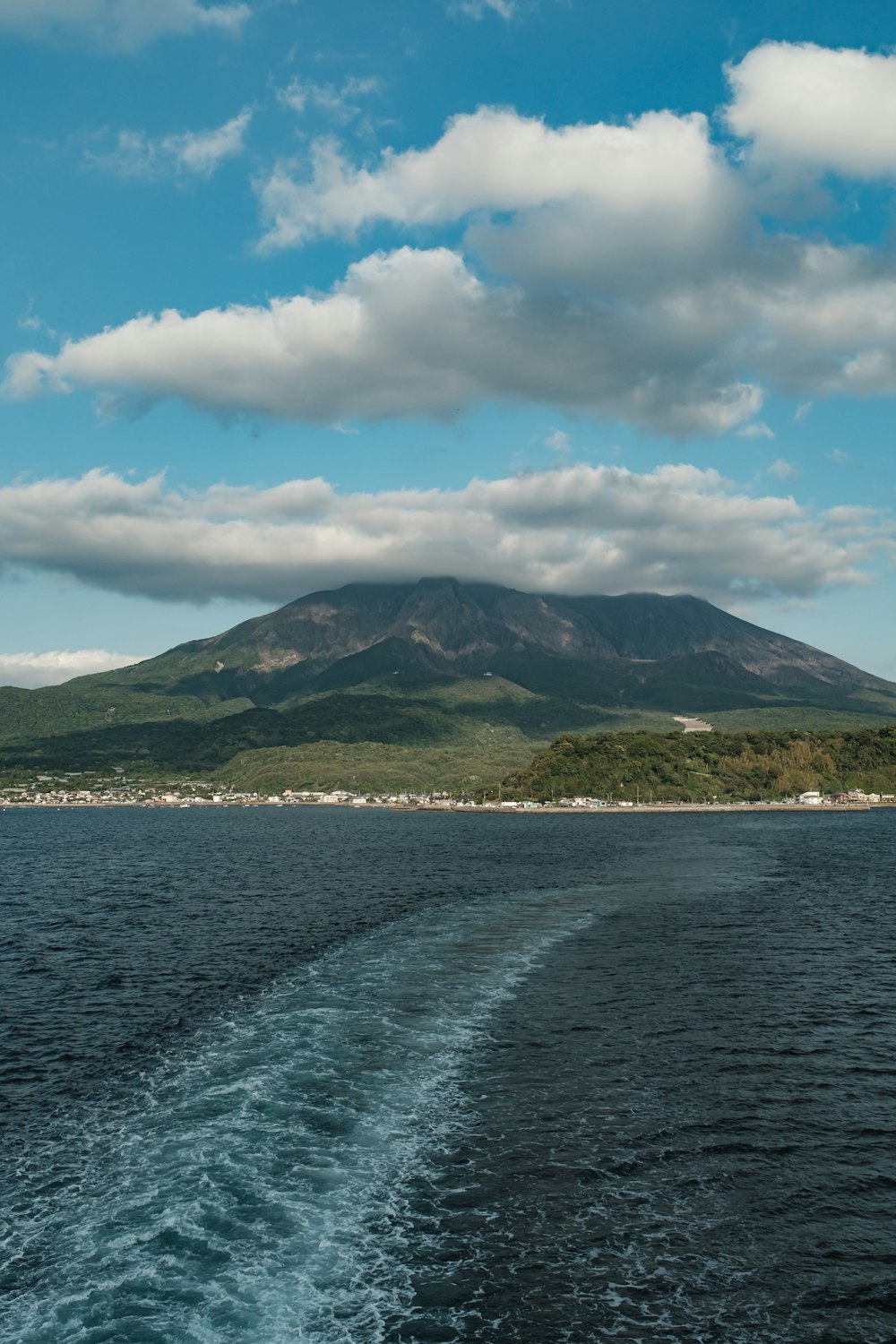 green mountain beside body of water under blue sky and white clouds during daytime