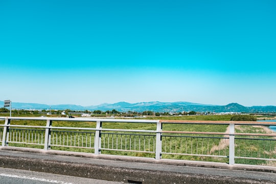 green grass field near mountain under blue sky during daytime in Kumamoto Japan