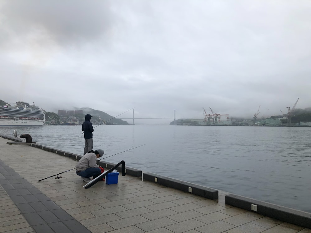 person in blue jacket and black pants standing on blue wooden dock during daytime