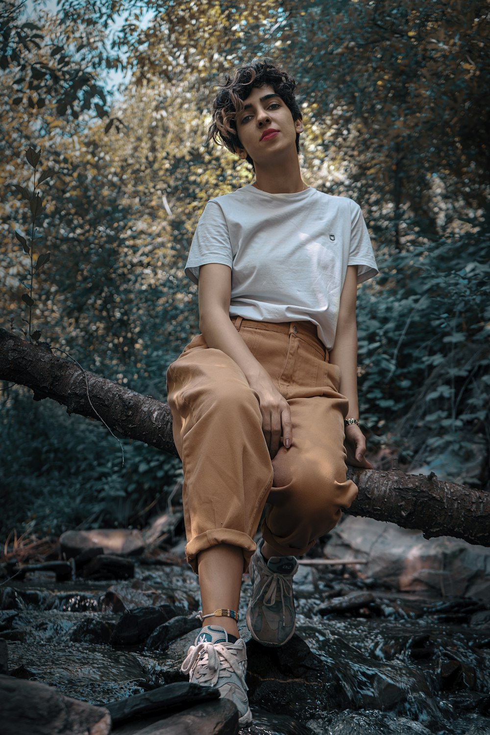 woman in white crew neck t-shirt and brown pants sitting on tree branch during daytime