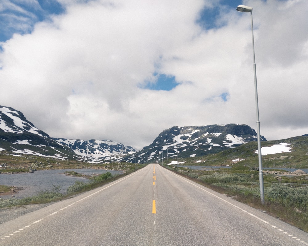 gray concrete road near snow covered mountain under cloudy sky during daytime