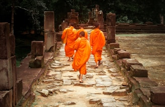 man in orange robe walking on gray concrete pathway during daytime
