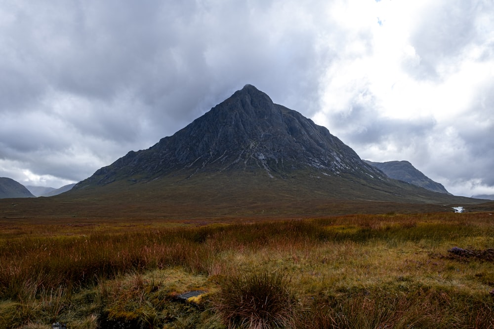 green and brown grass field near mountain under white clouds during daytime