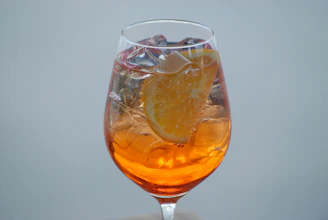 A vibrant glass of orange punch with fresh orange slices and ice cubes, glowing against a dark background.