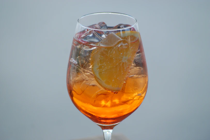 A vibrant glass of orange punch with fresh orange slices and ice cubes, glowing against a dark background.