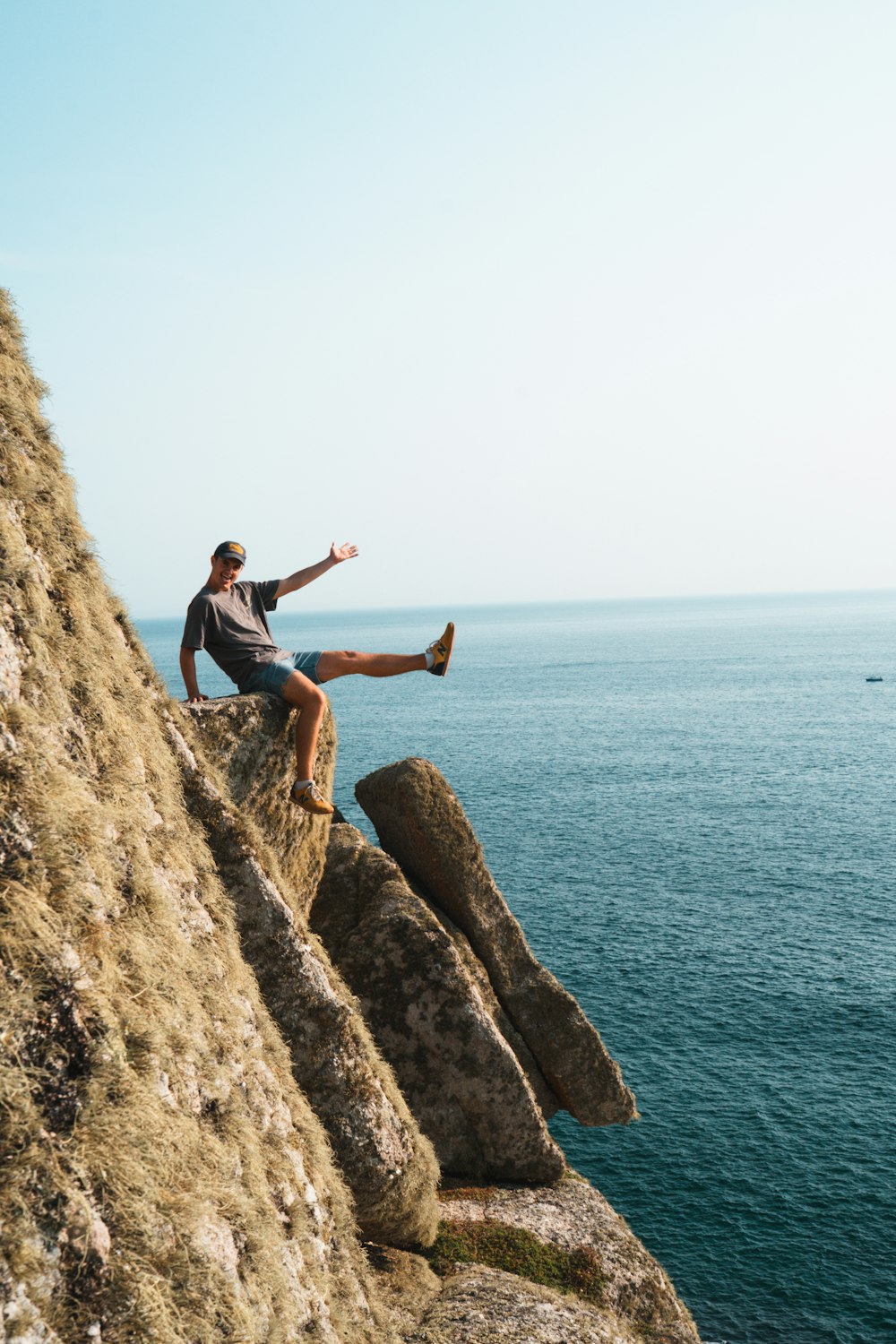 man in black t-shirt and black shorts sitting on brown rock formation near body of on on on on