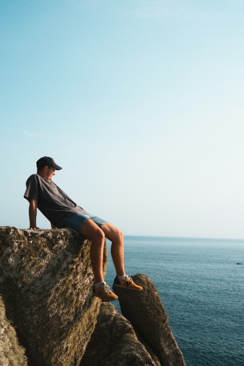 woman in gray t-shirt and blue denim shorts sitting on brown rock formation during daytime