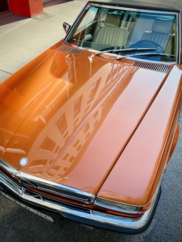 A sleek orange car gleaming under soft sunlight after a detailed cleaning and polish.