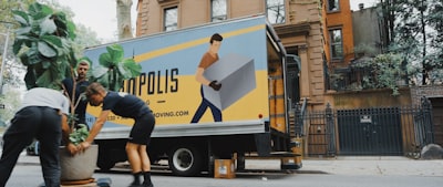 woman in blue shorts and black boots standing beside yellow and white truck during daytime moving teams background