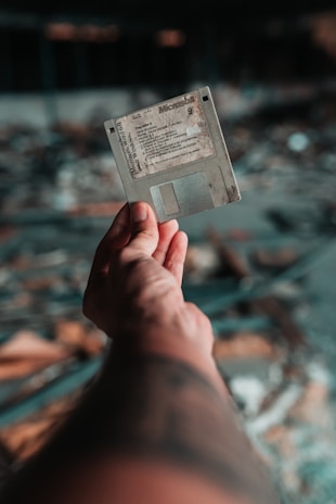 A hand holding a vintage floppy disk, contrasting with modern tech gear nearby.