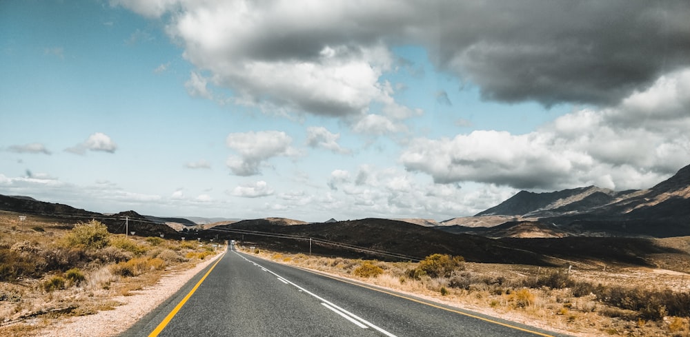 Carretera de hormigón gris cerca de Brown Mountain bajo nubes blancas durante el día