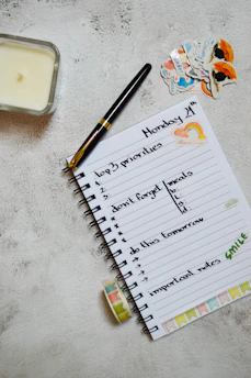 Close-up of a gold-accented planner and pen resting on a black leather notebook beside a glowing candle.