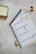 A neatly arranged journal or planner lays open on a textured surface. It has handwritten notes listing 'top 3 priorities', 'don't forget meals', 'do this tomorrow', and 'important notes'. A black and gold pen rests on the open page. Nearby are decorative stickers with colorful designs. A candle is placed to the left and a roll of washi tape lies near the notebook.