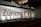 A modern building facade featuring large glass panels and a brightly illuminated interior. The word 'Zürich' is displayed prominently across the glass. The interior appears minimalist and well-lit, with visible structural elements and reflections on the glass surface.