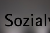 The image features a close-up of the word 'Sozialy' printed in bold black letters on a plain, light gray background. The lighting creates a subtle gradient effect on the background.