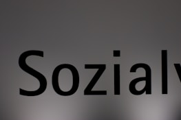 The image features a close-up of the word 'Sozialy' printed in bold black letters on a plain, light gray background. The lighting creates a subtle gradient effect on the background.