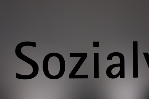 The image features a close-up of the word 'Sozialy' printed in bold black letters on a plain, light gray background. The lighting creates a subtle gradient effect on the background.