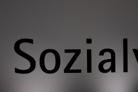 The image features a close-up of the word 'Sozialy' printed in bold black letters on a plain, light gray background. The lighting creates a subtle gradient effect on the background.