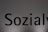 The image features a close-up of the word 'Sozialy' printed in bold black letters on a plain, light gray background. The lighting creates a subtle gradient effect on the background.