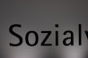 The image features a close-up of the word 'Sozialy' printed in bold black letters on a plain, light gray background. The lighting creates a subtle gradient effect on the background.