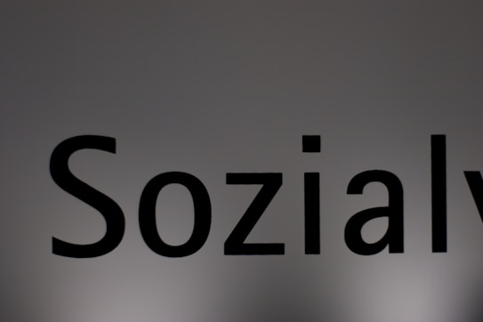 The image features a close-up of the word 'Sozialy' printed in bold black letters on a plain, light gray background. The lighting creates a subtle gradient effect on the background.