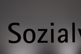 The image features a close-up of the word 'Sozialy' printed in bold black letters on a plain, light gray background. The lighting creates a subtle gradient effect on the background.