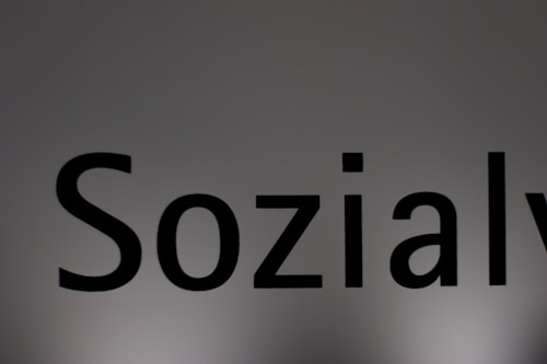 The image features a close-up of the word 'Sozialy' printed in bold black letters on a plain, light gray background. The lighting creates a subtle gradient effect on the background.