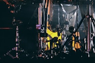 An intricate arrangement of metallic drum hardware. Chrome drum stands and hoops are illuminated by dim, moody lighting with a contrasting yellowish glow in the background.