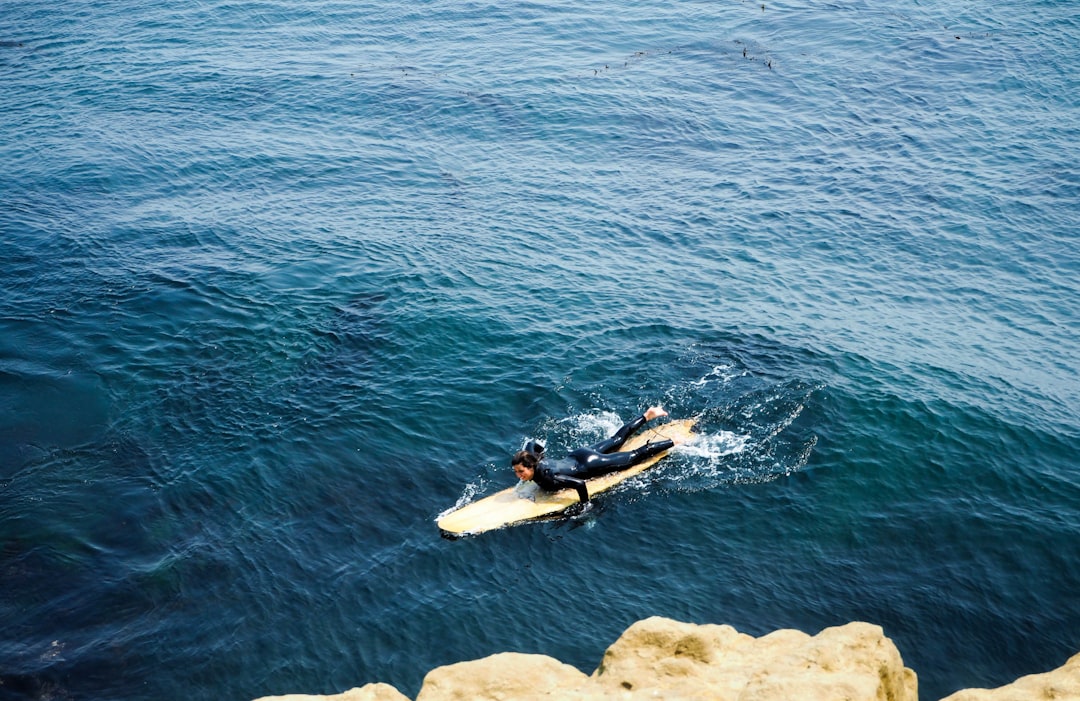 man in black wetsuit riding white surfboard on blue sea during daytime