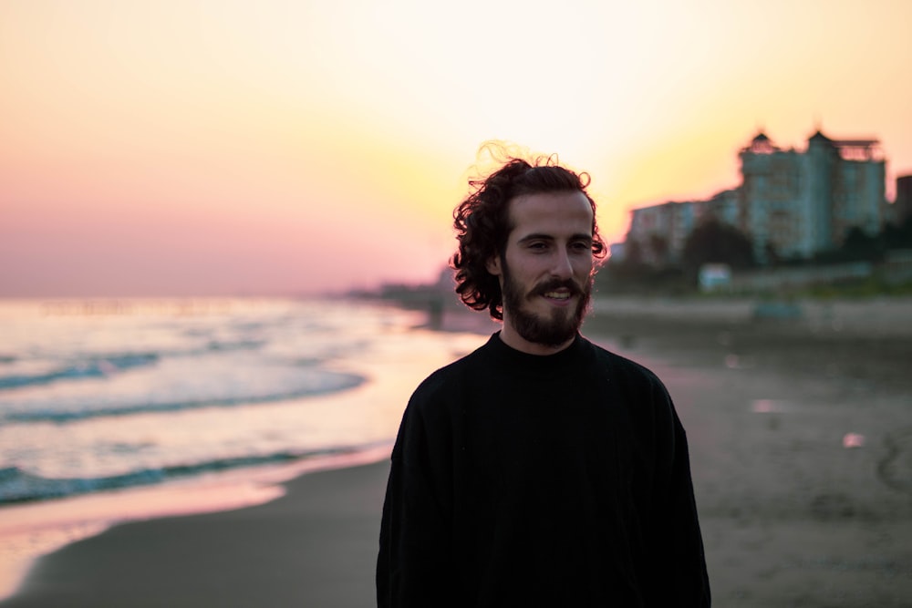 man in black sweater standing near body of water during sunset