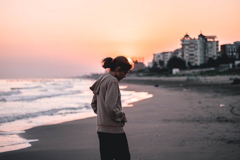 woman in gray hoodie standing on beach during sunset