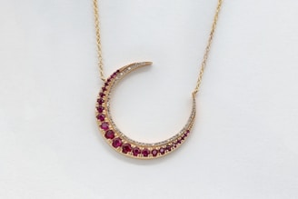 Elegant gold necklace with a crescent moon pendant on a white marfil background.