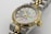 A luxury wristwatch featuring a mother-of-pearl dial adorned with diamond hour markers and gold accents. The watch has a two-tone design with a polished metal bracelet and a prominent gold bezel. The brand name and additional text are engraved on the dial.