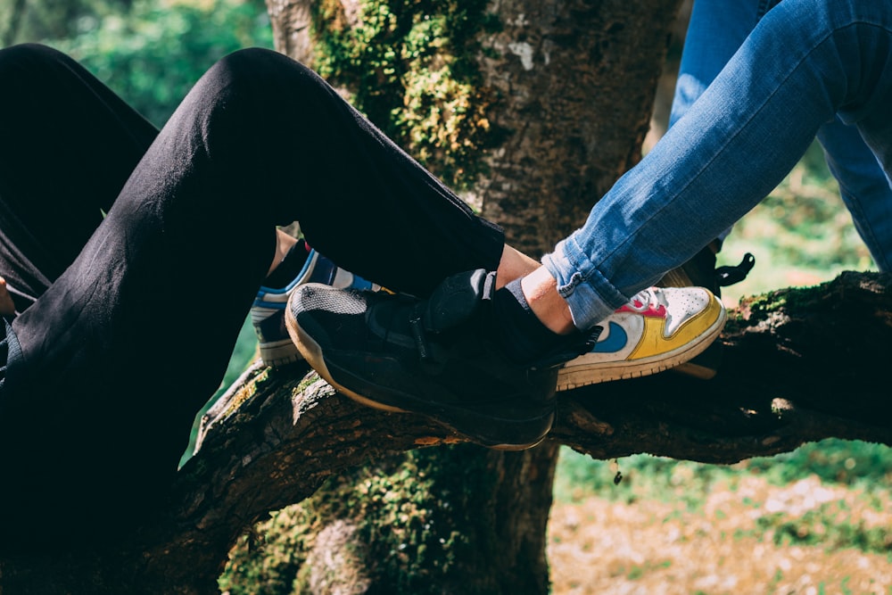person in black pants and black and white nike sneakers sitting on brown tree log