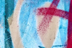 Abstract painting featuring vibrant splashes of red across a textured blue and beige background. The composition includes bold, sweeping lines and speckles that add depth.