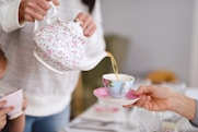 person holding white and pink floral ceramic teapot