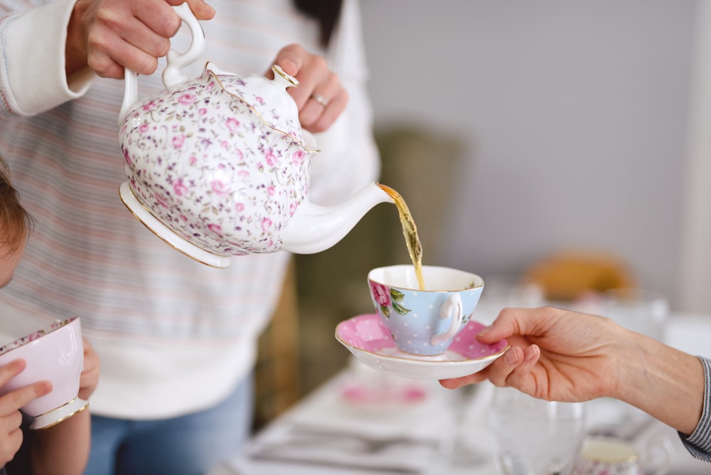 person holding white and pink floral ceramic teapot