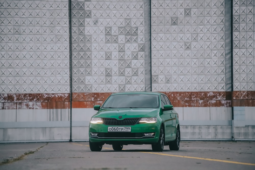 green car parked beside white brick wall