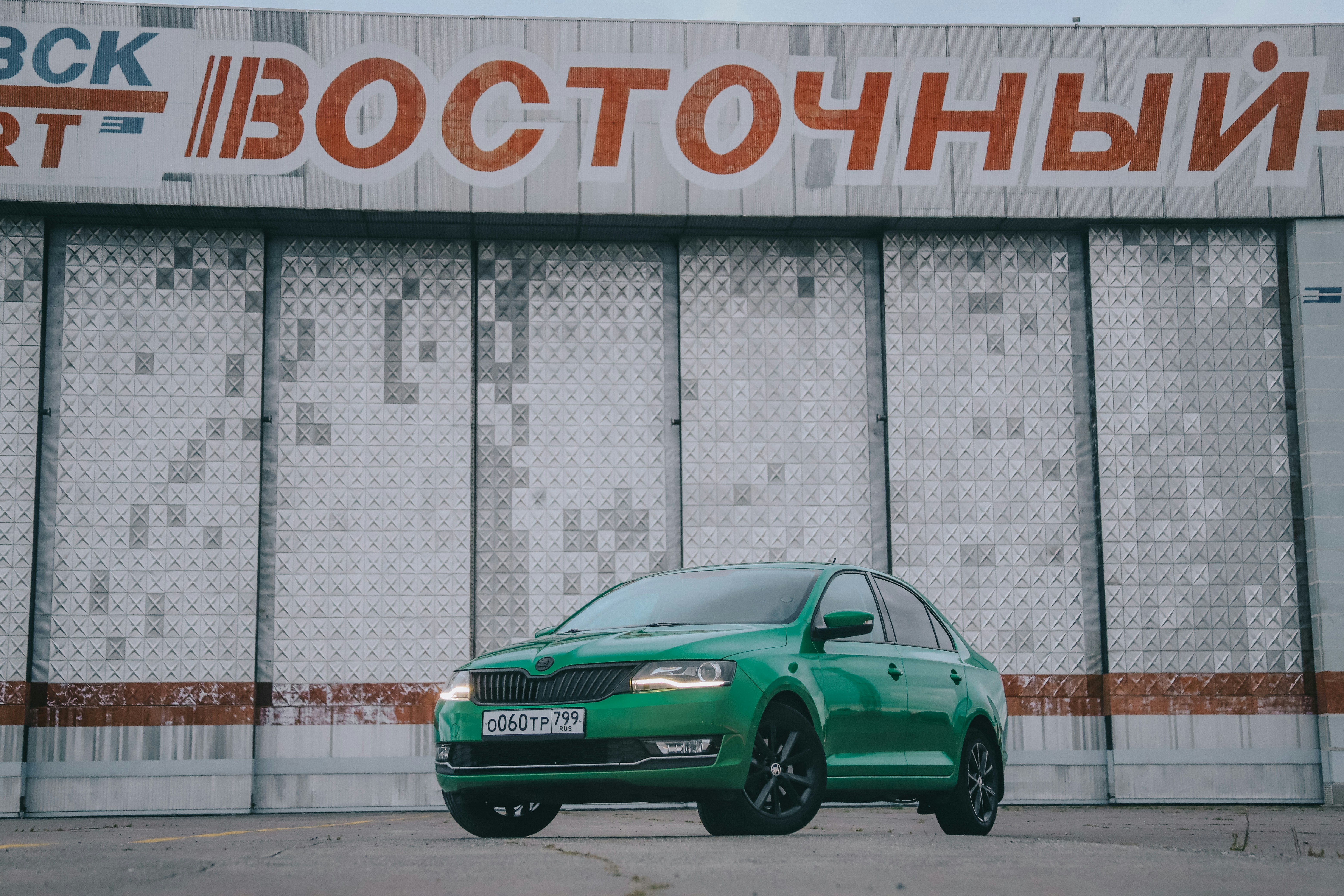 green sedan parked beside gray concrete wall skoda teams background