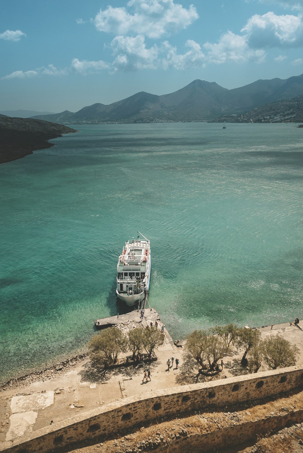 white and blue boat on sea near brown mountain during daytime