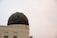 An observatory with a large, dark-colored dome sits atop a classical-style building. The building features intricate detailing and multiple rectangular windows. The sky appears overcast.