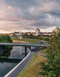 brown concrete building near green trees and river under cloudy sky during daytime