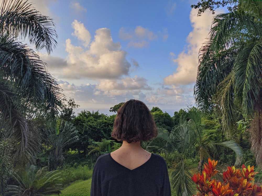 Mujer con camisa negra de pie cerca del campo de hierba verde bajo el cielo nublado azul y blanco durante