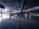 A dimly lit, empty underground parking lot with concrete surfaces and rows of orange-colored pillars. The ceiling has exposed pipes and lighting fixtures, and the open space is devoid of vehicles or people.