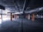 A dimly lit, empty underground parking lot with concrete surfaces and rows of orange-colored pillars. The ceiling has exposed pipes and lighting fixtures, and the open space is devoid of vehicles or people.